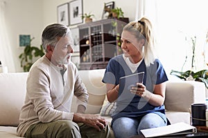 Female healthcare worker sitting with a senior Hispanic man in his living room during a home visit