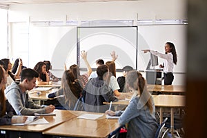 Female High School Teacher Asking Question Standing By Interactive Whiteboard Teaching Lesson