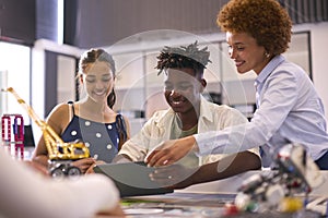 Female High School Teacher With Digital Tablet Helping Students In STEM Technology Lesson