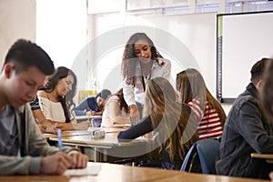 Female High School Teacher Standing By Student Table Teaching Lesson