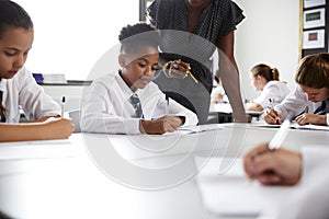 Female High School Tutor Helping Students Wearing Uniform Seated Around Tables In Lesson