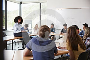 Female High School Tutor Sitting At Table With Pupils Teaching Maths Class photo