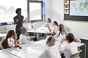 Female High School Tutor Standing By Tables With Students Wearing Uniform Teaching Lesson photo