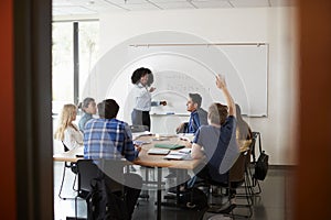 Female High School Tutor At Whiteboard Teaching Maths Class With Pupil Asking Question