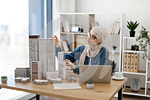 Female in hijab replacing building models on office desk