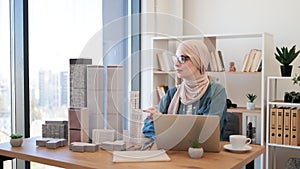 Female in hijab replacing building models on office desk