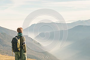 Female hiker with backpack looking at the majestic view on the italian Alps. Mist and fog in the valley below, snowcapped mountain