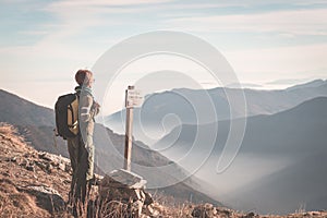 Female hiker with backpack looking at the majestic view on the italian Alps. Mist and fog in the valley below, snowcapped mountain