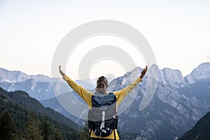 Female hiker with a backpack standing with her arms spread wide looking at a beautiful view of high mountains