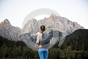 Female hiker with backpack standing and looking at a beautiful view of high mountains