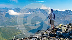 Female hiker in blue jacket overlooking vast arctic mountain landscape from the top of the mountain. Top of Naite, Sarek