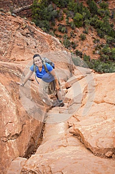 Female hiker climbing a steep red rock cliff