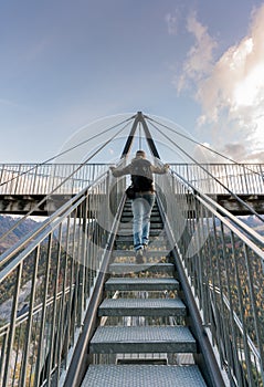 Female hiker climbing up metal stairs that lead up to an impressive lookout and viewpoint platform in the Grisons near Flims in S
