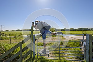 Female hiker climbs over a fence with a special step for walkers