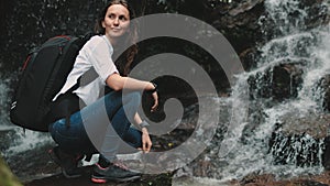 Female hiker crouch near wild splashing waterfall