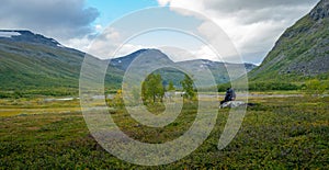 Female hiker with heavy gear sitting on a boulder, overlooking vast Arctic valley Rapadalen in Sarek National Park