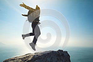 Hiker jumping on sunrise seaside cliff edge