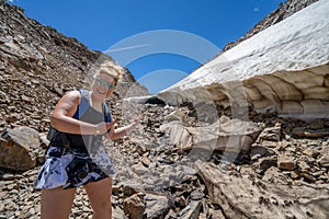 Female hiker points and smiles at a large ice cave along a trail