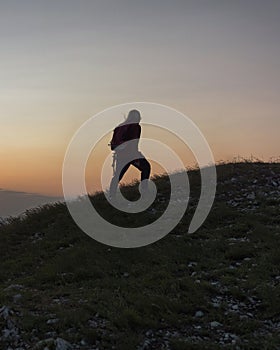 Female hiker silhouette walking the trail uphill, at sunset