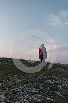 Female hiker silhouette walking the trail uphill, at sunset