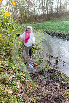 Female hiker standing on banks of stream with her dachshund on muddy ground