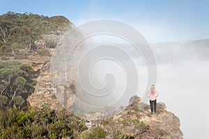 Female hiker standing on a rock pinnacle with rising fog from valley
