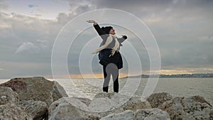 Female hiker standing on a sea cliff, arms outstretched, gazing at the stunning view of cold ocean waves.