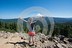 Female hiker stands on the summit of Tom and Harry Mountain in Mt. Hood National Forest, with her arms held up, looking at Mo