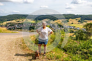 Female hiker tourist standing next her dog on hill, German countryside landscape in background