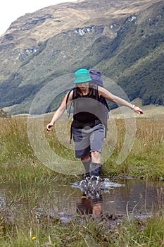 Female hiker wading thru a creek while tramping in New Zealand