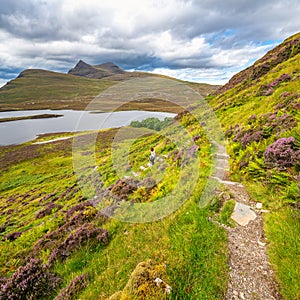 Female hiker walking along a path between mountains, lochs and valleys, in Scotland, UK.