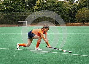 Female hockey player attacking and hitting on a grass field