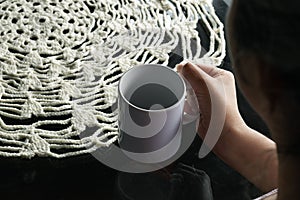 Female holding a cup of coffee with a book with blank pages, and a crocheted centerpiece tablecloth