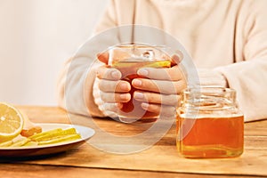 Female holding a cup of hot tea with citrus, ginger and honey - home treatment