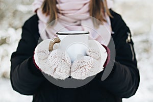 Female holding a cup of tea on winter picnic in the woods. Woman hand`s in a warm pink knitted gloves