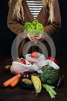 Female holding fresh salad among organic healhty food in plastic free eco bags over black background. Waste free