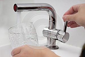 Female holding glass at water tap and filling water with lead contamination