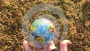 Female holding global earth in her hand, against yellow grass, ecology concept, human impact, save the planet