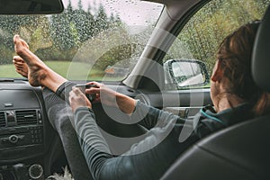 Female holding the hot tea tourist thermos mug. She sitting on co-driver seat inside modern car, putting her legs on car dashboard photo