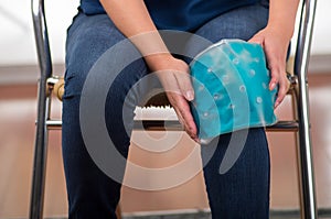 Female holding ice gel pack on knee, medical concept, in office background