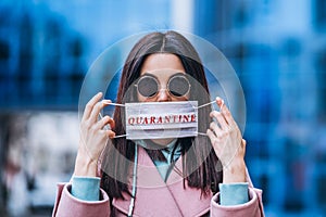 Female holding medical mask outdoors in the city with the quarantine inscription on it. Health protection and prevention of virus