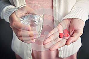 Female is holding red pills in heart shape.