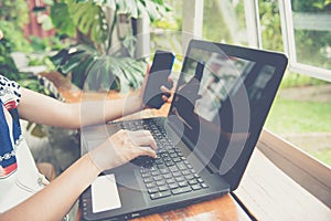 female holding smartphone getting message with confirmation making transaction on laptop computer