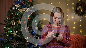 Female holding smartphone in hands and using mobile. Blurry Christmas lights in background. Adult woman texting sms