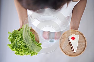 Female holding vegetable dishes and cakes thinking of choosing to eat which is more beneficial to the body. Weight loss concept,