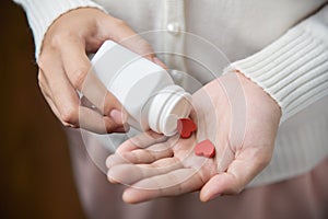 Female holding a white pill bottle and red pills in heart shape.