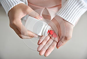 Female holding a white pill bottle and red pills in heart shape.