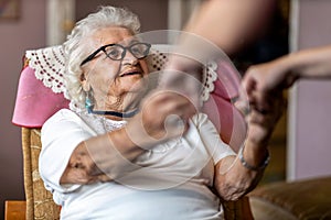 Female home carer supporting old woman to stand up from the armchair