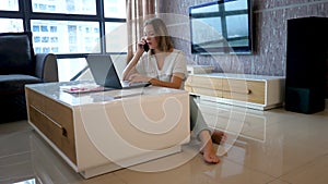 Female home worker has telephone conversation and inputs data in laptop computer