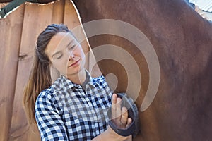 Female Horse Owner Cleaning Neck Of Her Bay Horse In The Stable During Daytime